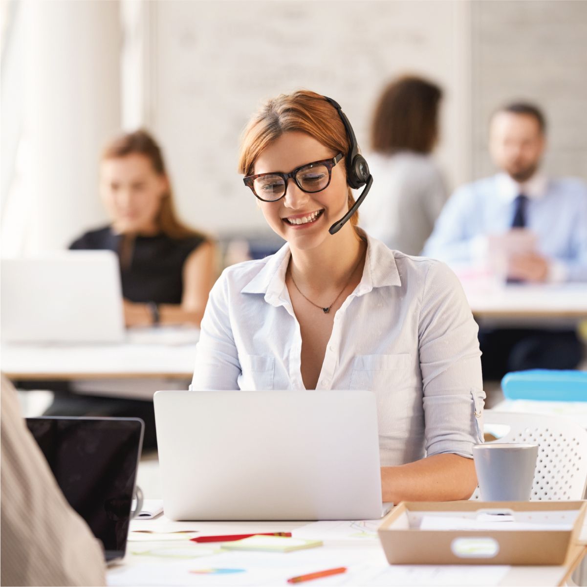 Frau arbeitet am Laptop und telefoniert währendessen mit ihrem Headset
