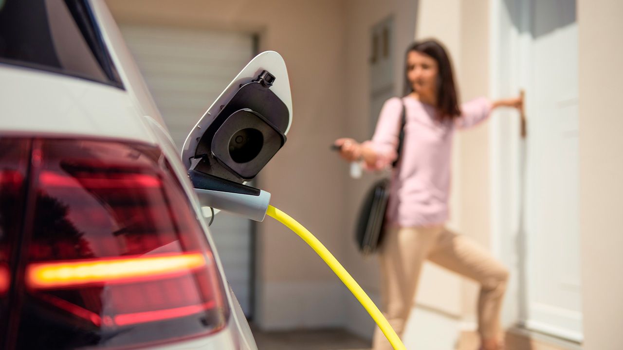 E-Auto lädt in der Einfahrt, während Frau durch die Tür ins Haus geht