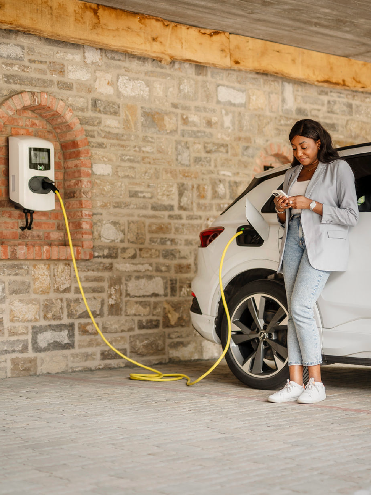 Frau schaut aufs Handy beim Laden eines E-Autos