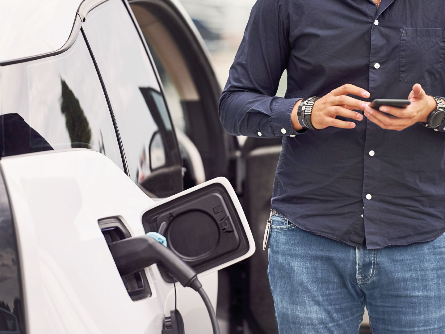 Mann checkt sein Handy, während sein E-Auto lädt