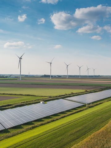 Solarpark mit Solarmodulen und Windraedern und Feldern im Hintergrund 