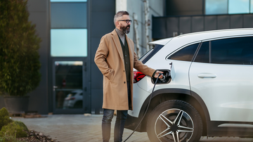Mann in Mantel laedt E-Auto