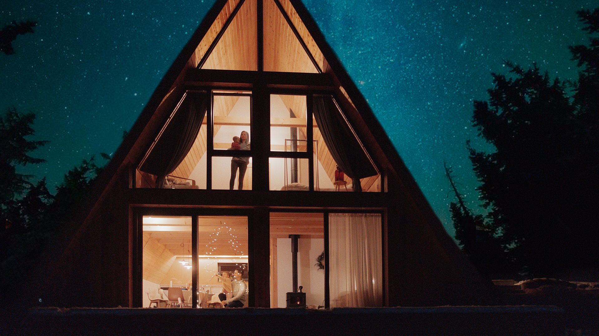beleuchtete Finnhütte im Wald bei Nacht mit Sternenhimmel