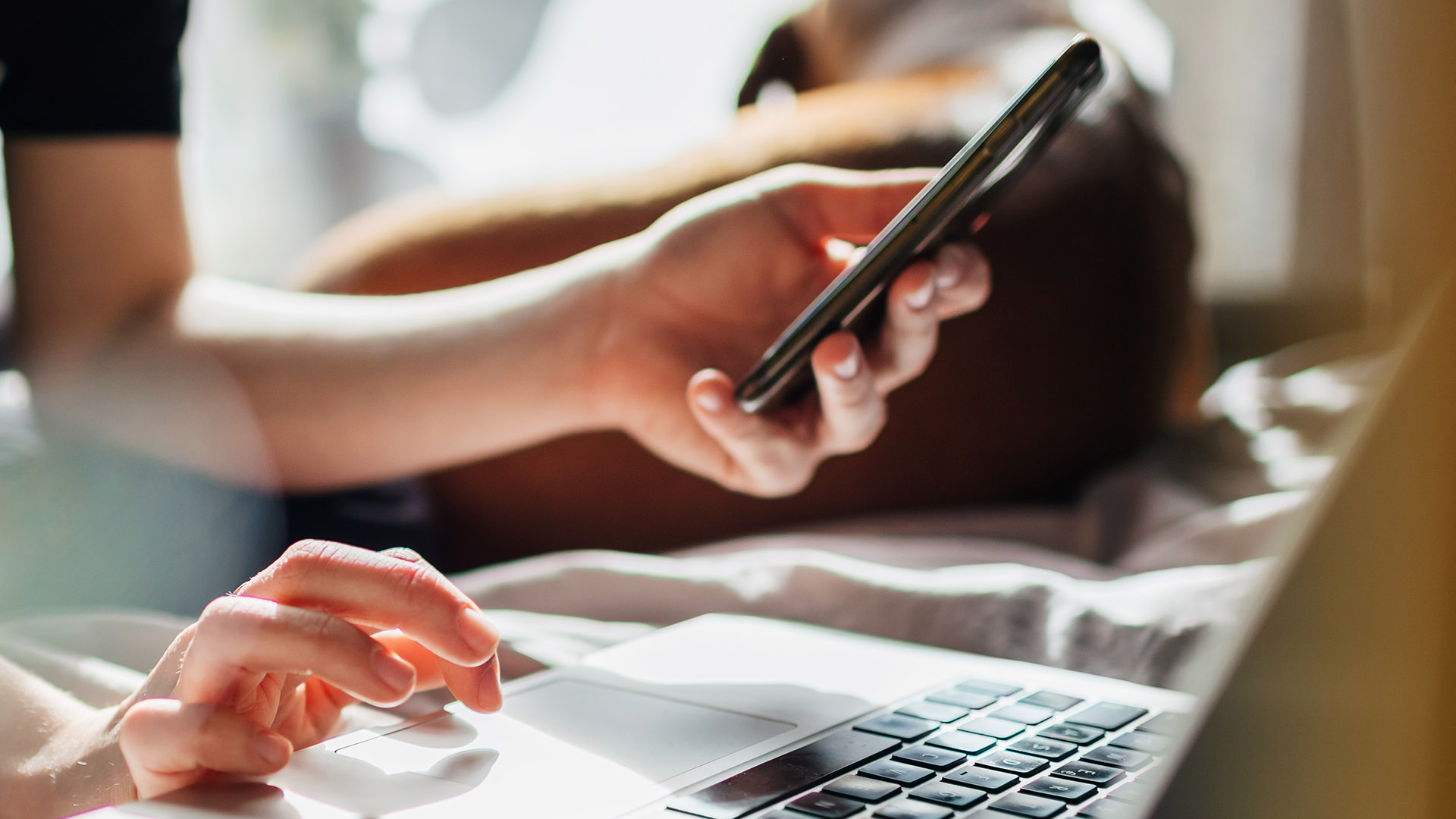 Frau sitzt am Laptop und hält Handy in der Hand