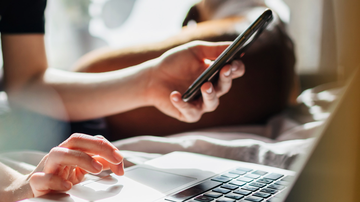 Frau sitzt am Laptop und hält Handy in der Hand
