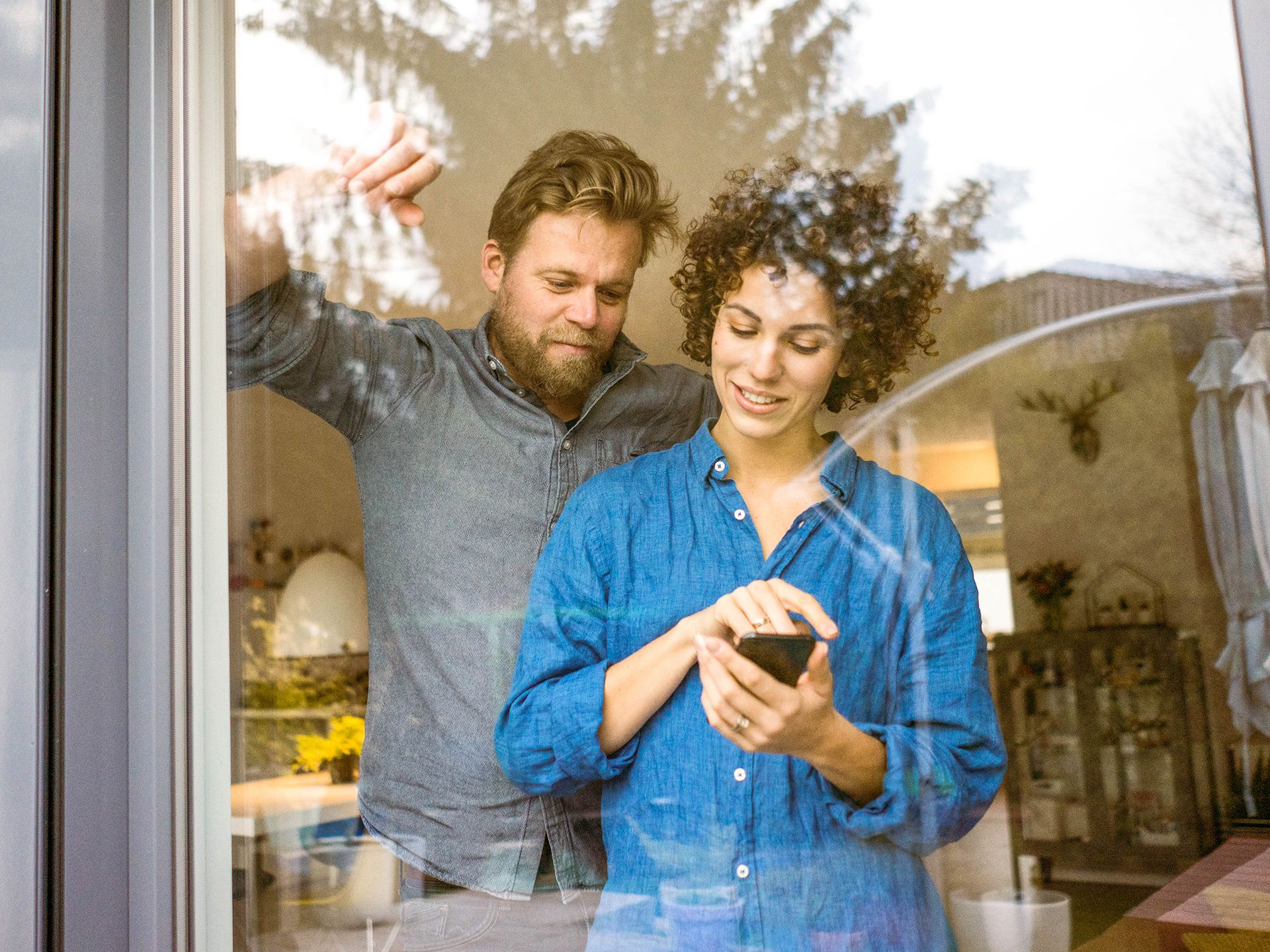 Paar steht vor Wohnzimmerfenster und schaut aufs Handy