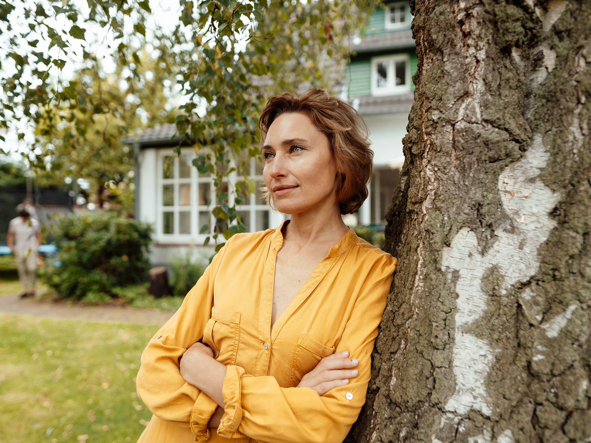 Frau lehnt am Baum und schaut in die Ferne