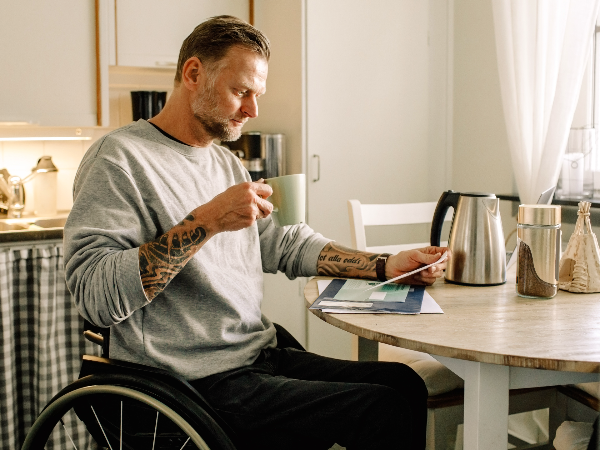 Mann im Rollstuhl sitzt am Tisch und trinkt Kaffee