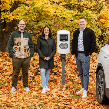 Mehrere Prsonen stehen vor Schnellladesauele im Hintergrund Herbstlaub