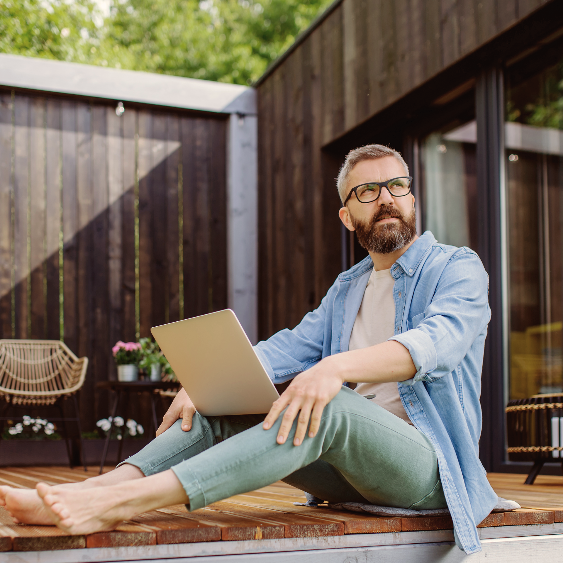 bärtiger Mann mit Brille und Laptop im Freien, barfuß