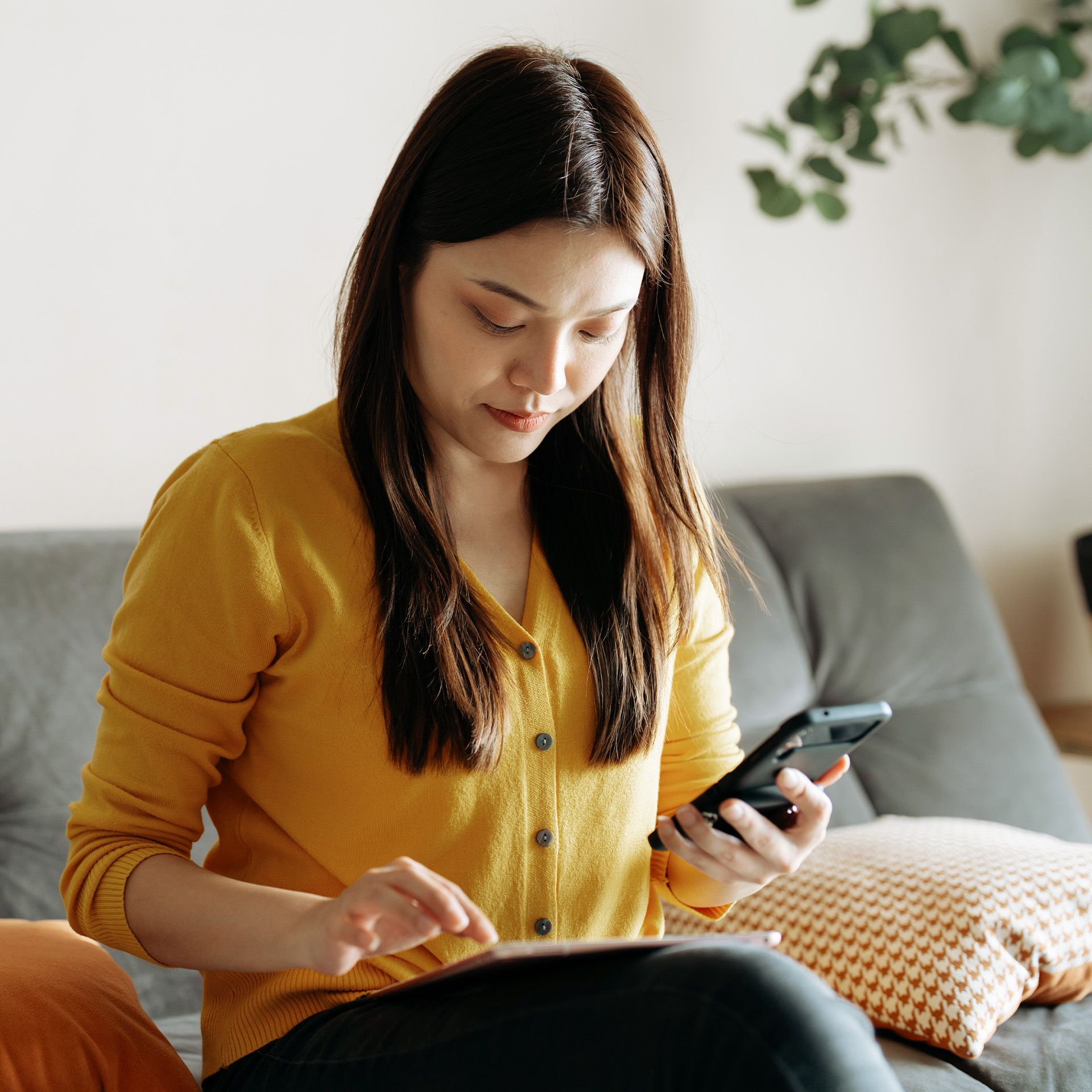 Frau sitzt auf dem Sofa mit Handy in der Hand