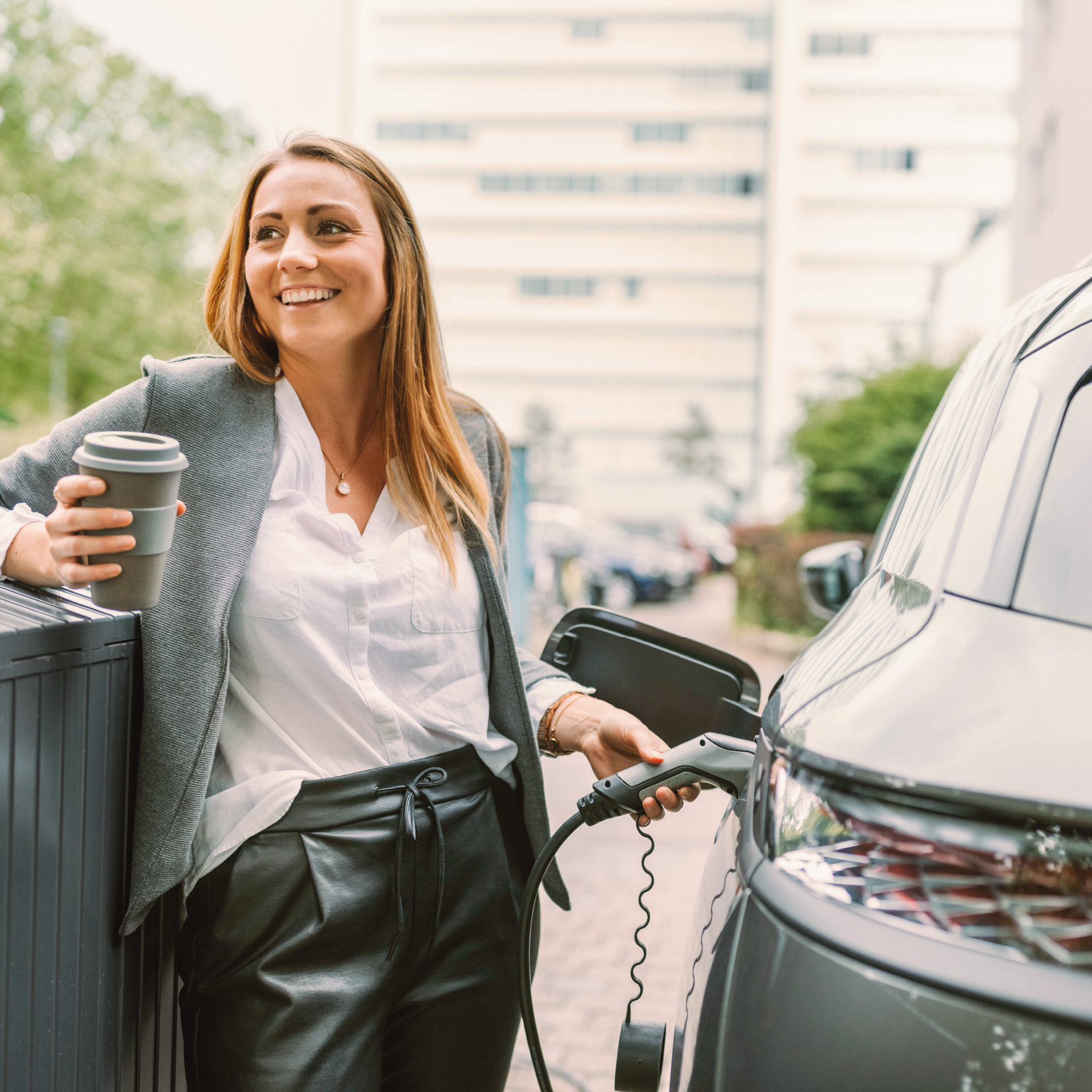 Frau mit Kaffee in der Hand lädt E-Auto