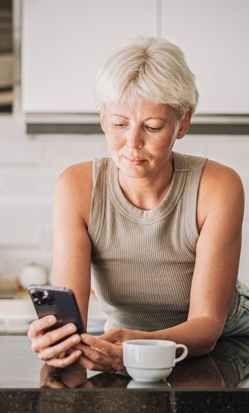 Frau in der Kueche guckt aufs Handy