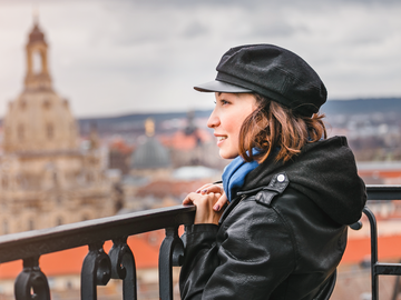 Frau mit Muetze steht an Bruestung und schaut ueber die Stadt