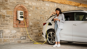 Frau lehnt an E-Auto an Ladestation