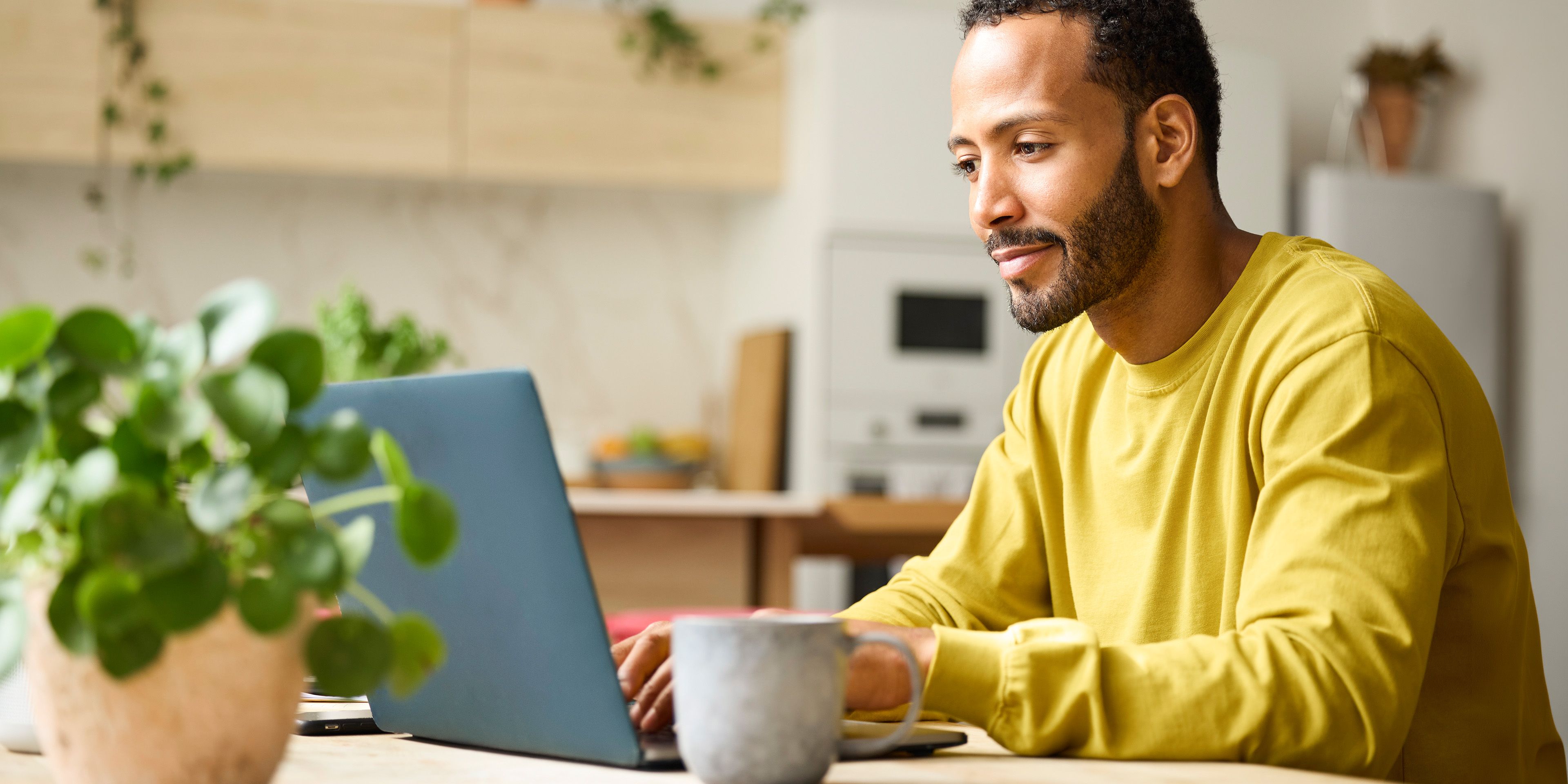 Mann in gelben Pullover sitzt am Laptop