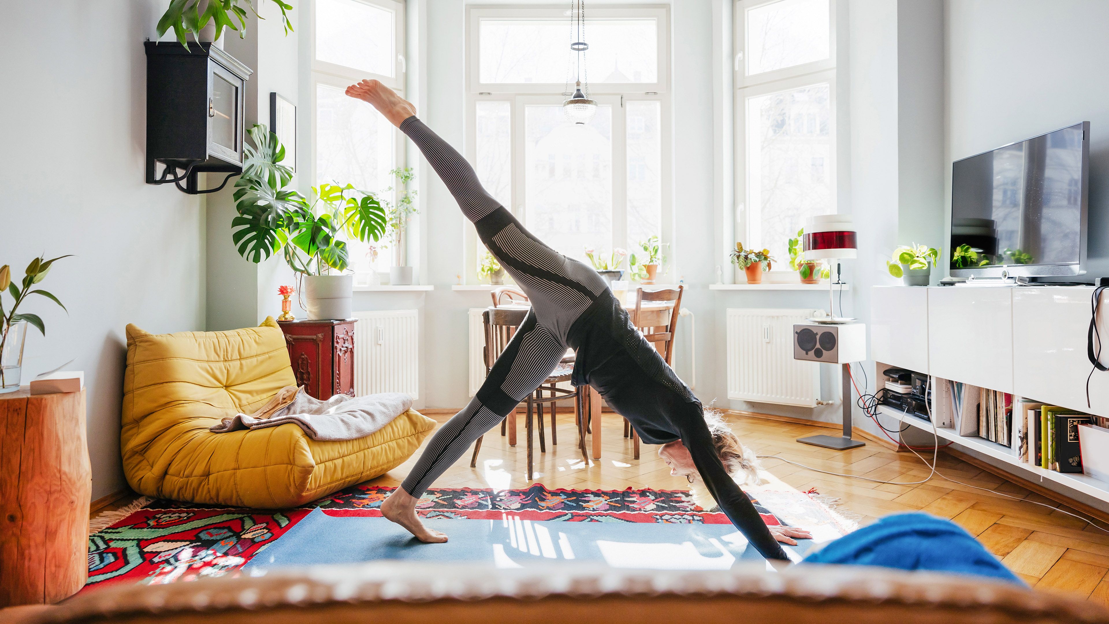 Frau in Yogapose: Strom sparen im Wohnzimmer
