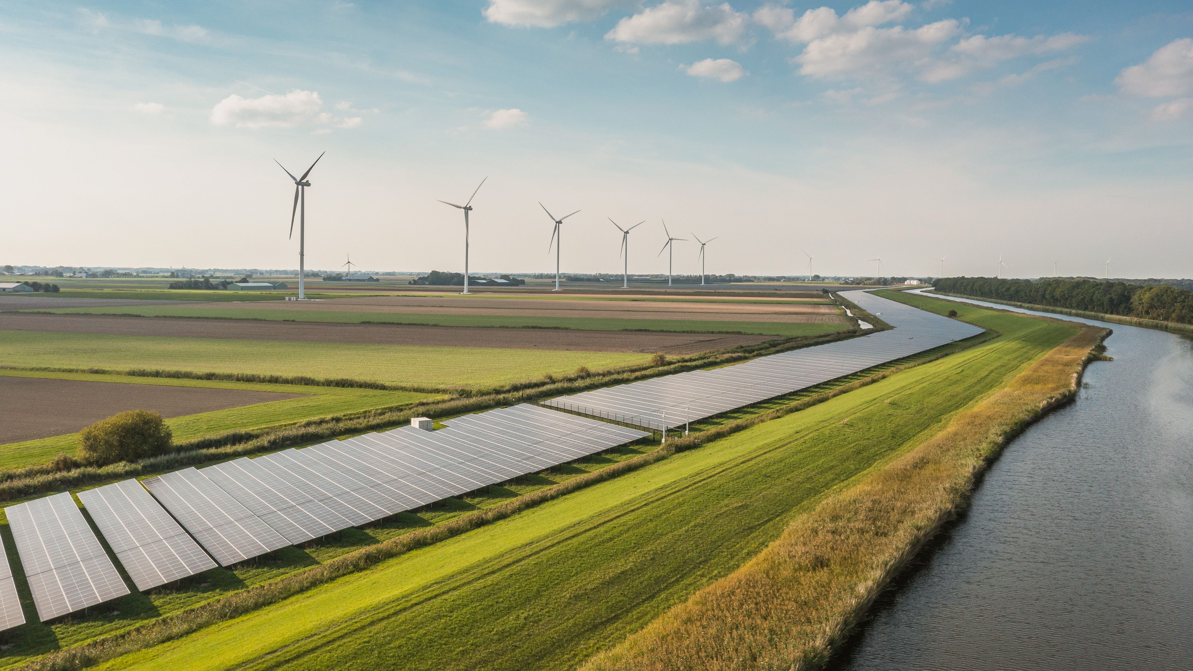 Solarpark mit Solarmodulen und Windraedern und Feldern im Hintergrund 