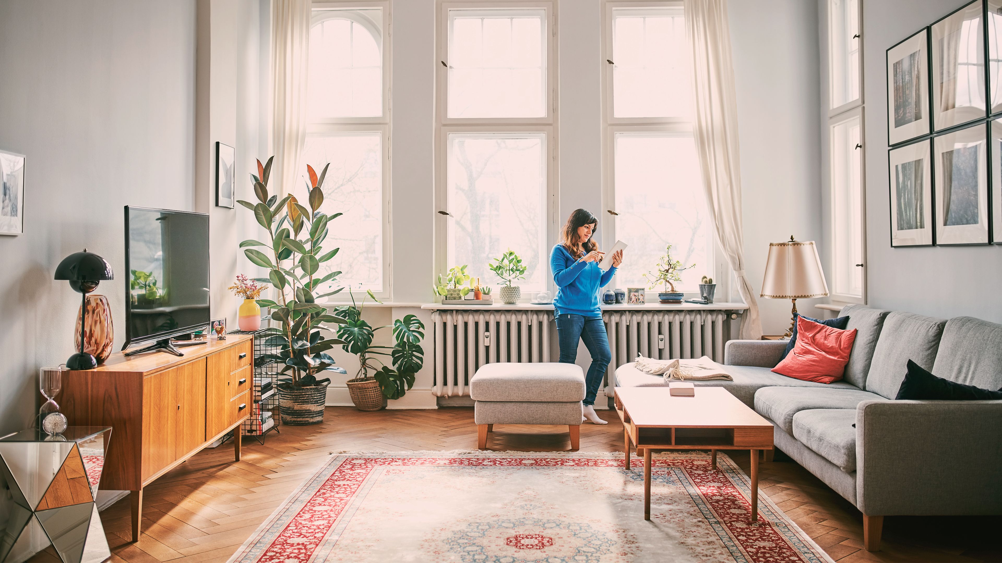 Frau sthet vor der Heizung im Wohnzimmer und schaut auf ihr Handy