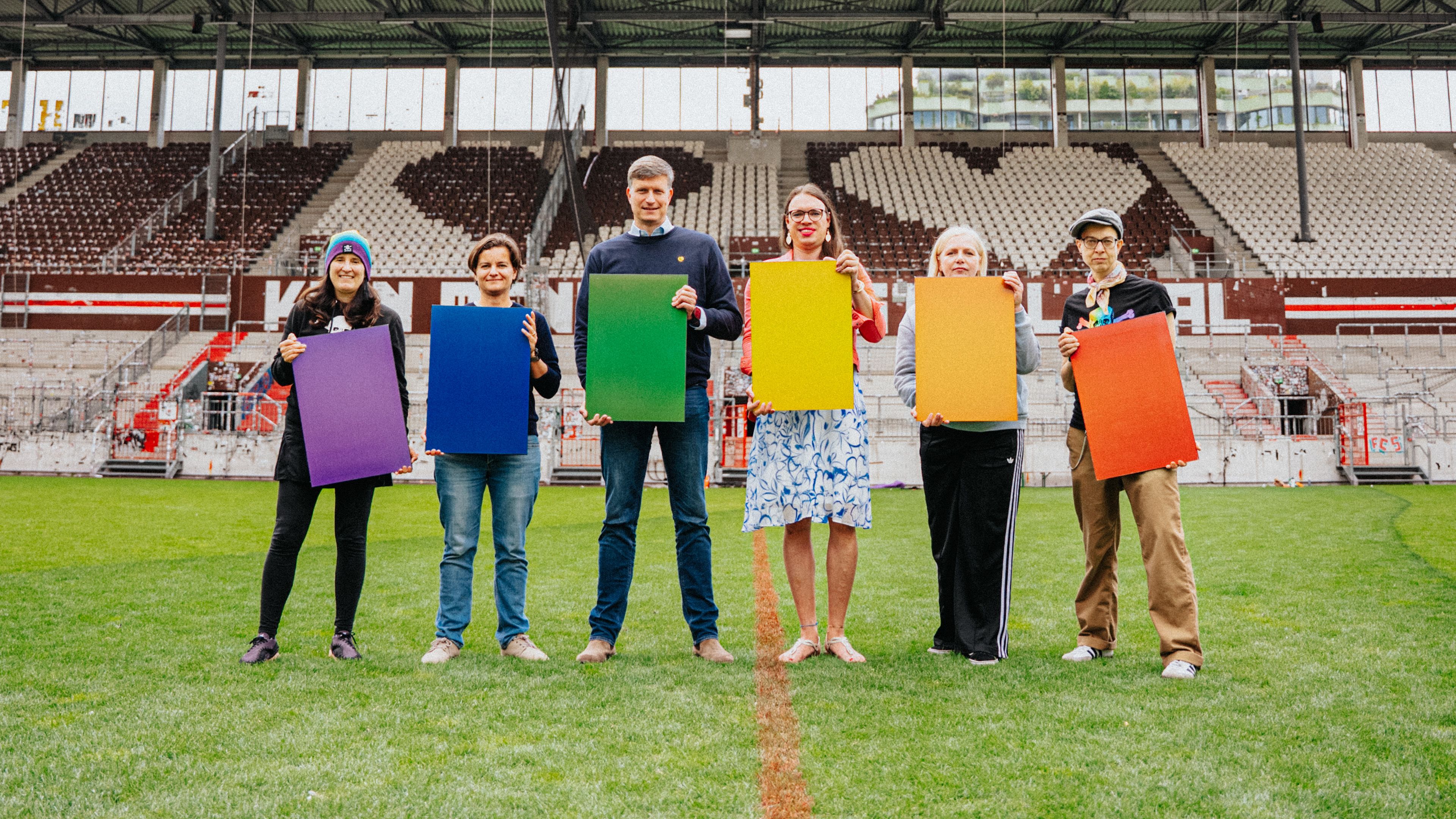 Sechs Menschen halten bunte Solarpanele in einem Stadion in den Haenden