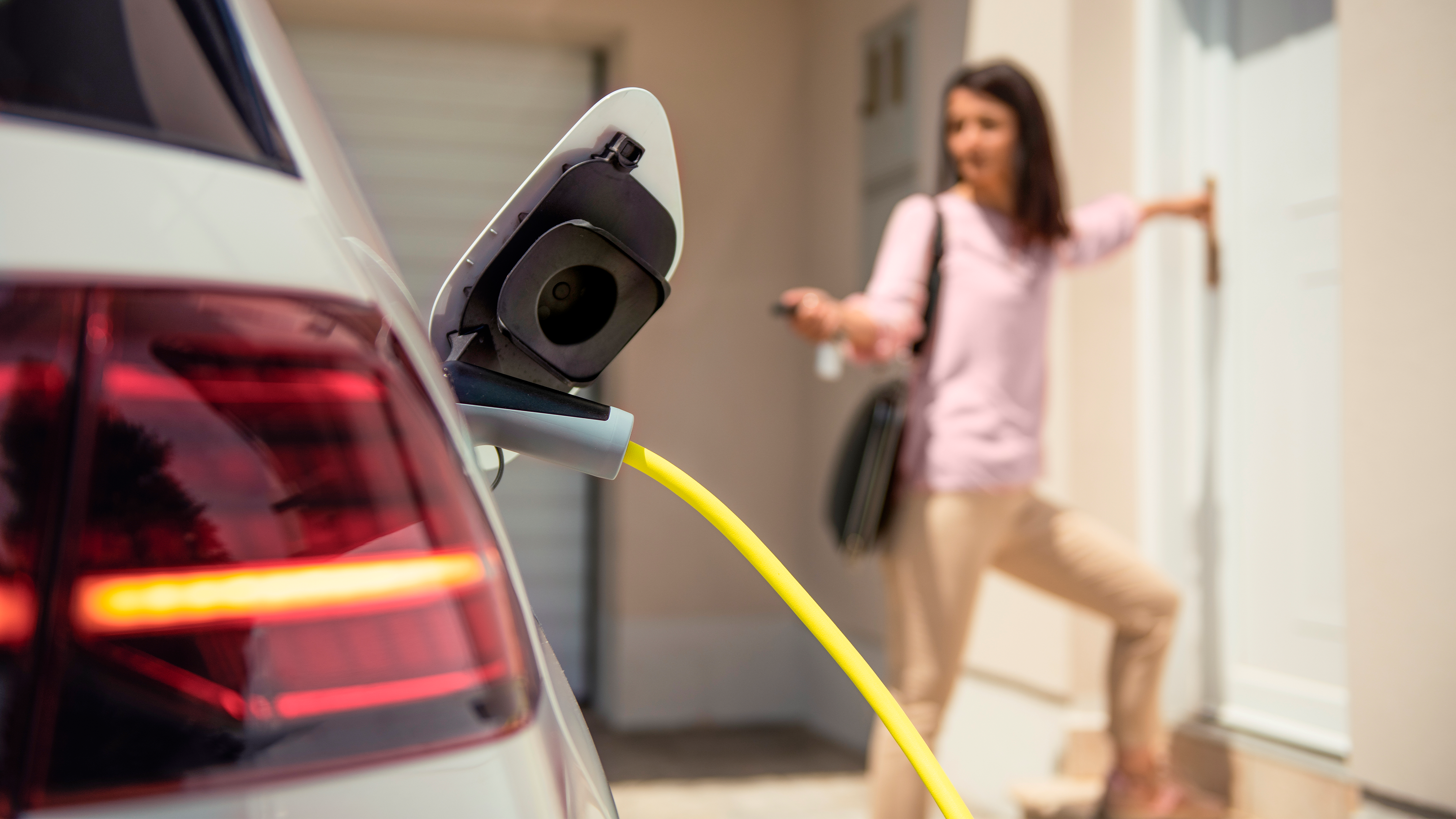 E-Auto lädt in der Einfahrt, während Frau durch die Tür ins Haus geht