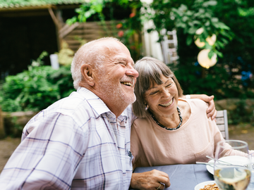 Altes Ehepaar sitzt lachend am Tisch