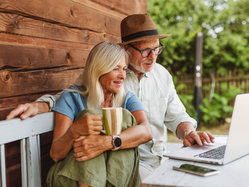 Altes Paar sitzt auf Bank und schaut auf Laptop