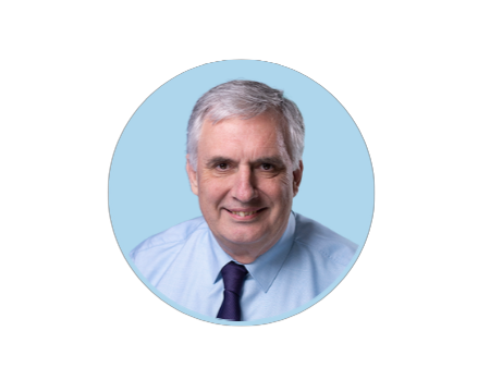 A man with gray hair in a light blue shirt and dark tie, smiling against a light blue background.