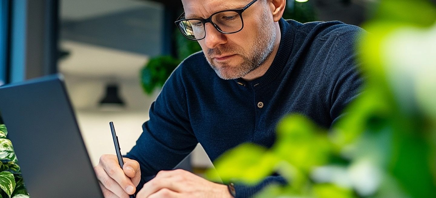 Muž pracující na notebooku a píšící poznámky v zeleném, moderním kancelářském prostředí