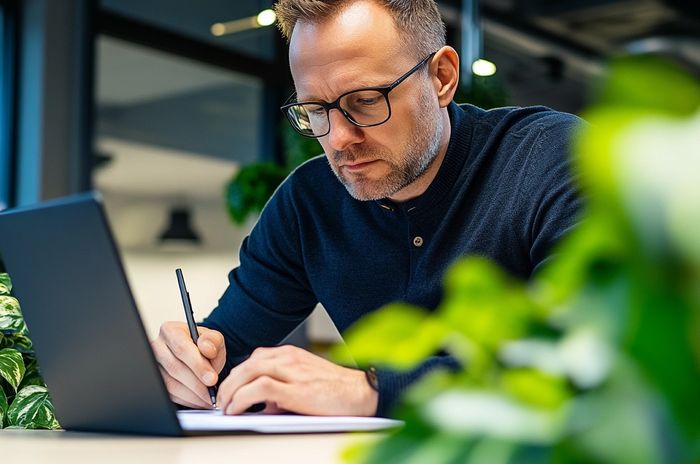 Muž pracující na notebooku a píšící poznámky v zeleném, moderním kancelářském prostředí
