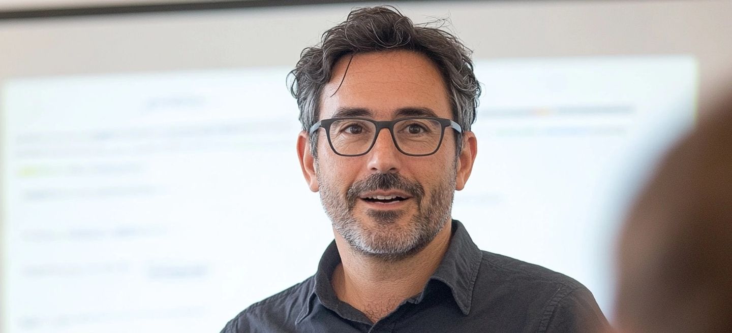 Hombre con gafas hablando durante presentación frente a pizarra