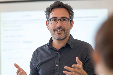 Hombre con gafas hablando durante presentación frente a pizarra