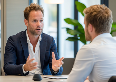 Manager in a suit talking to a colleague at a meeting table in a bright space with plants