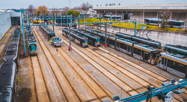 Aerial view of a STIB-MIVB tram depot in Brussels, with multiple trams parked on parallel tracks and maintenance operations taking place across the rail yard.