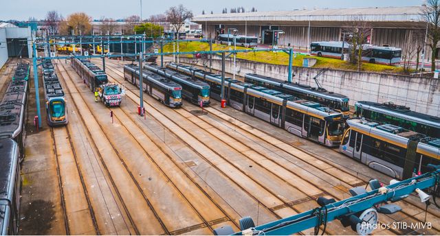 Aerial view of a STIB-MIVB tram depot in Brussels, with multiple trams parked on parallel tracks and maintenance operations taking place across the rail yard.