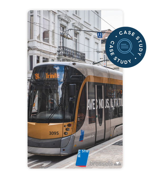 A modern tram in Brussels marked "Trinité," with a beige and black design, passes through an urban street with classic white buildings.