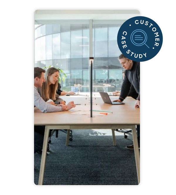Three people in an office meeting around a table, discussing papers, with a laptop in front of them. A "Customer Case Study" badge is in the corner.
