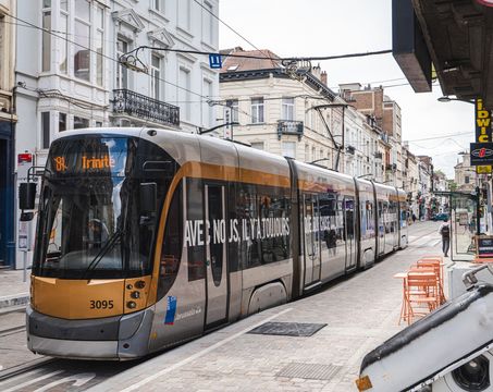 A modern STIB-MIVB tram travels through a narrow Brussels city street lined with historic buildings, shops, and cafés.