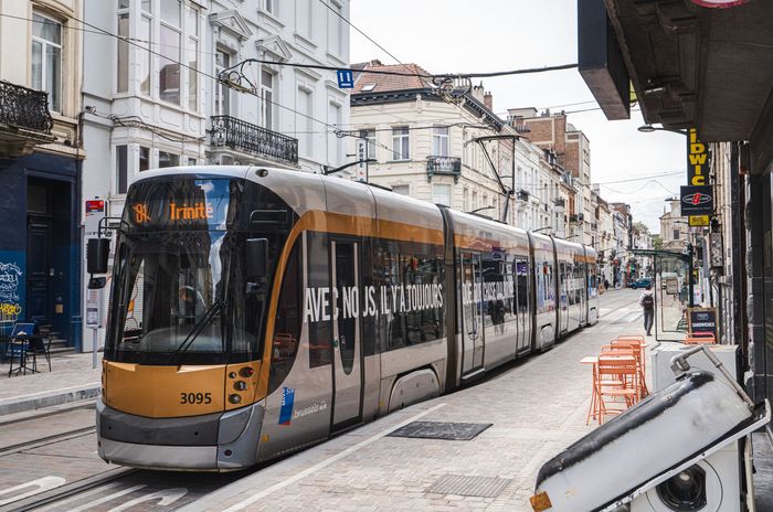 A modern STIB-MIVB tram travels through a narrow Brussels city street lined with historic buildings, shops, and cafés.