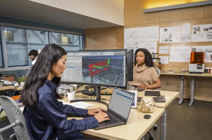 Two women collaborate at a workstation using Autodesk software to review project designs in a professional AEC environment.