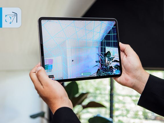 Person holding a tablet displaying a 3D scanned room with a grid overlay, showcasing augmented reality technology.