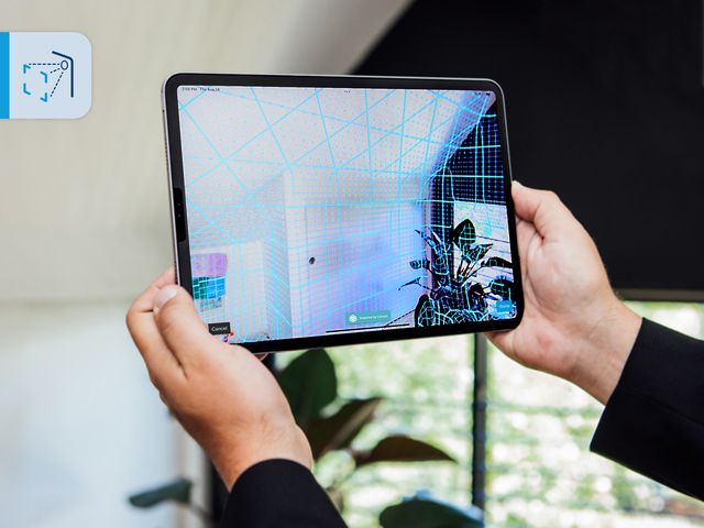Person holding a tablet displaying a 3D scanned room with a grid overlay, showcasing augmented reality technology.
