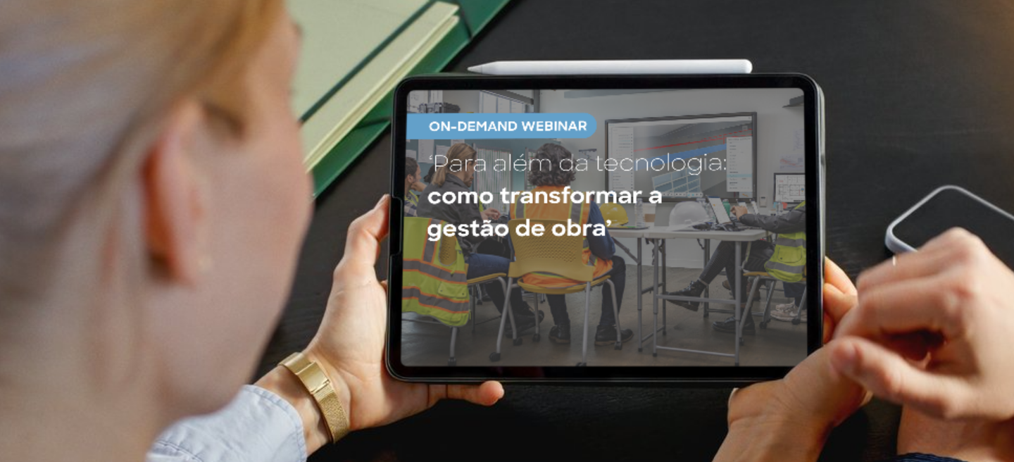 Person holding tablet displaying a webinar titled "Como transformar a gestão de obra" with construction workers shown on screen.