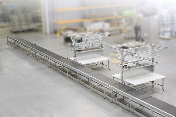 Industrial assembly line with metal frameworks and conveyor belt in a spacious, modern factory setting.