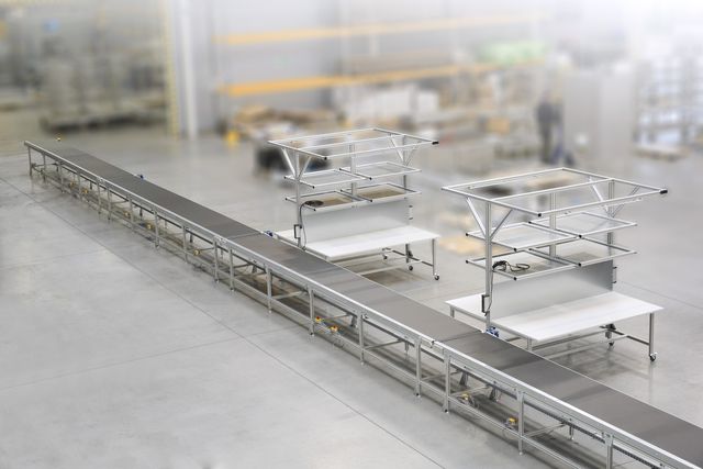 Industrial assembly line with metal frameworks and conveyor belt in a spacious, modern factory setting.