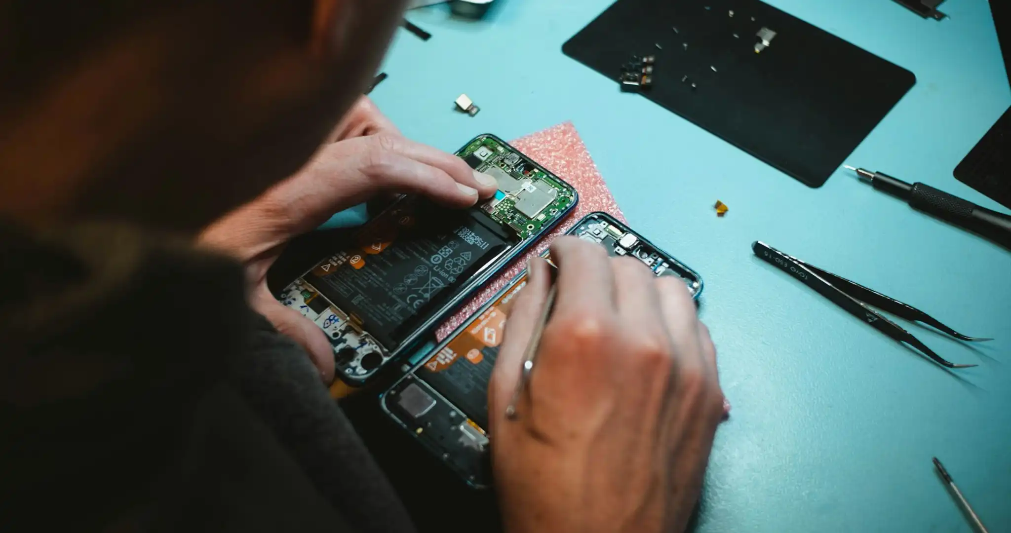 Person repairing a smartphone on a blue table, surrounded by tools and electronic components.