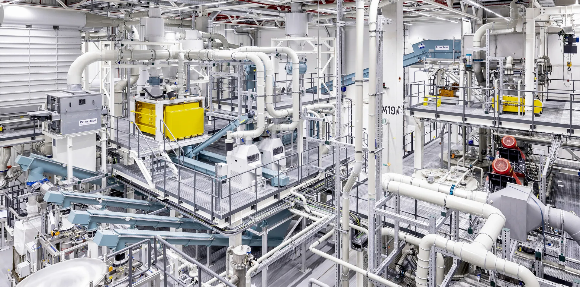 Innenansicht einer Industrieanlage von Mercedes-Benz mit weißen Rohrleitungen, Metallstrukturen und Maschinen in Gelb- und Türkistönen.