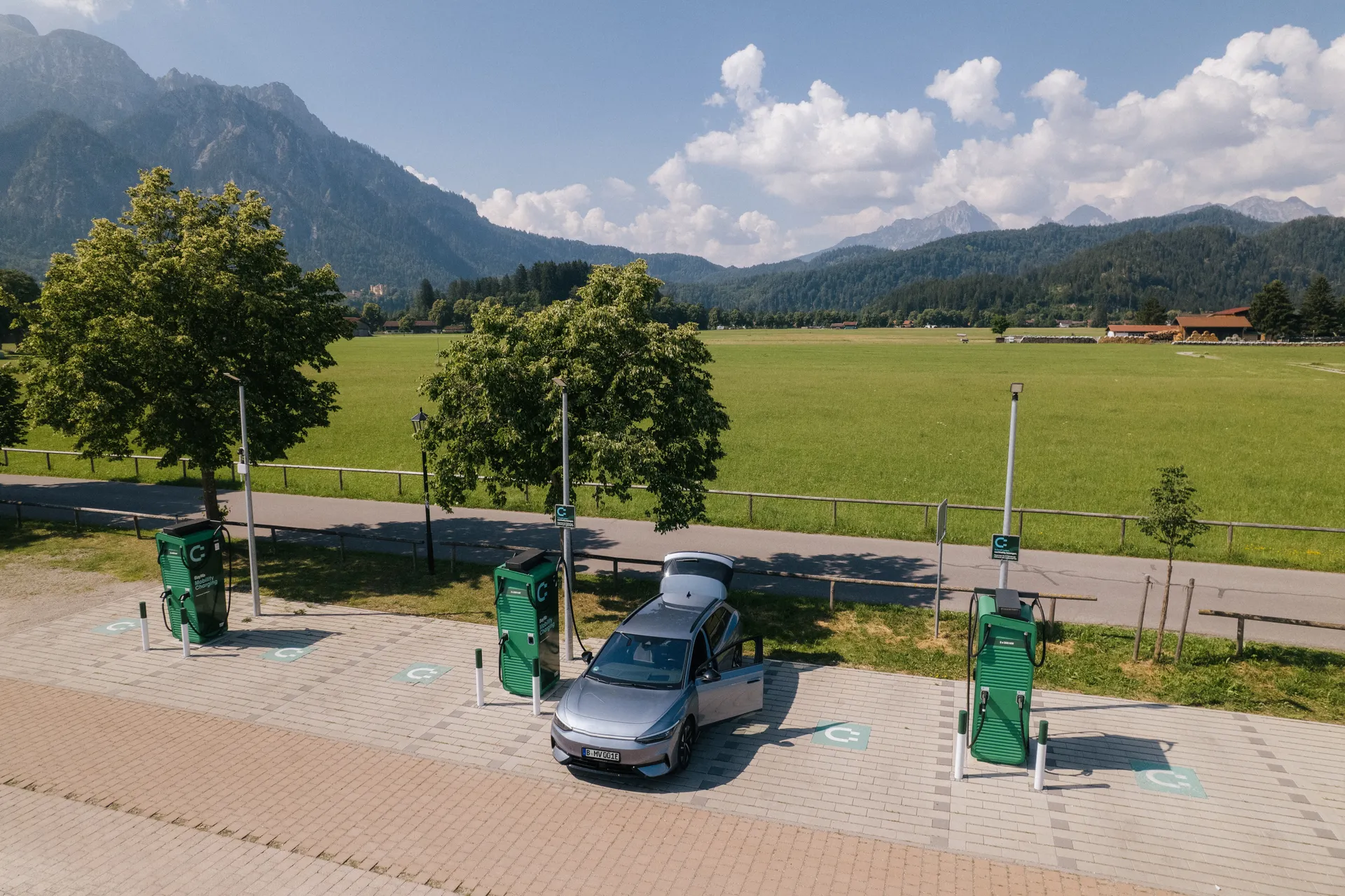 Ladepark mit drei grünen Ladesäulen von BayWa auf einem gepflasterten Platz. Ein silbernes E-Auto steht an der mittleren Säule und lädt.