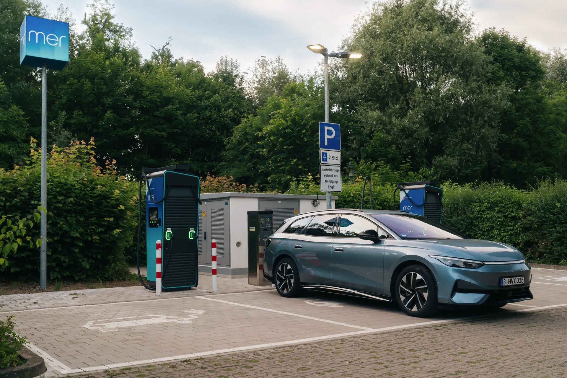 Blaues E-Auto steht an einer Ladestation von Mer Germany. Grüne Hecken im Hintergrund.