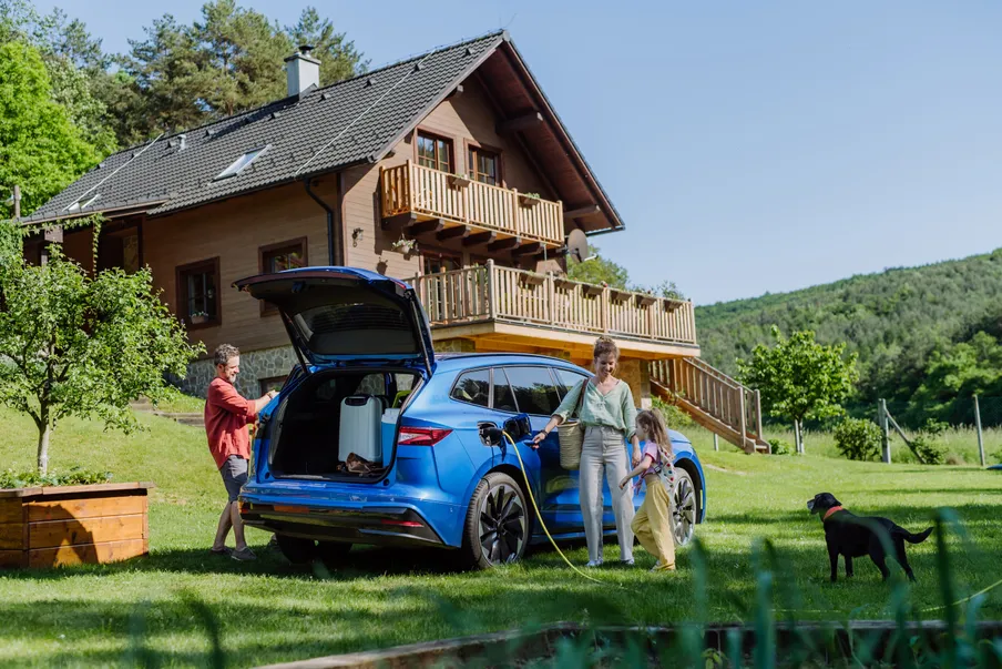 Eine Familie belädt ein Elektroauto mit Koffern. Das Auto ist an eine Ladestation angeschlossen.